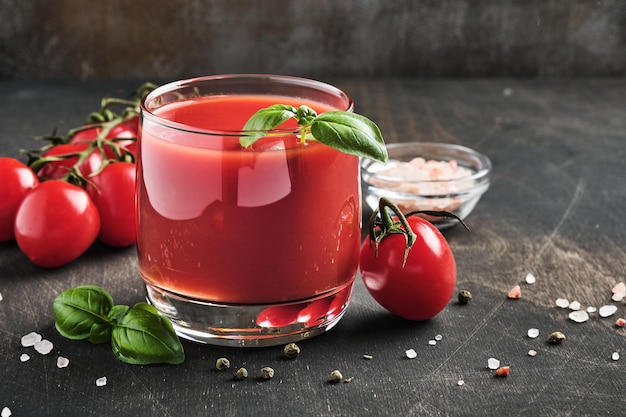 Vaso de jugo de tomate fresco, sal, albahaca y tomates en soporte de madera sobre fondo de madera vieja. Con espacio de copia.