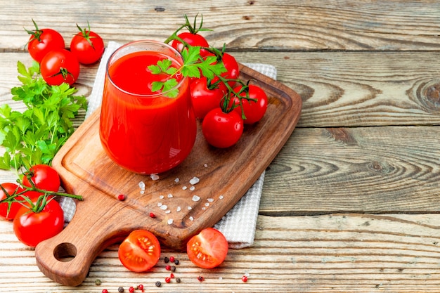 Vaso de jugo de tomate fresco y tomates en la madera