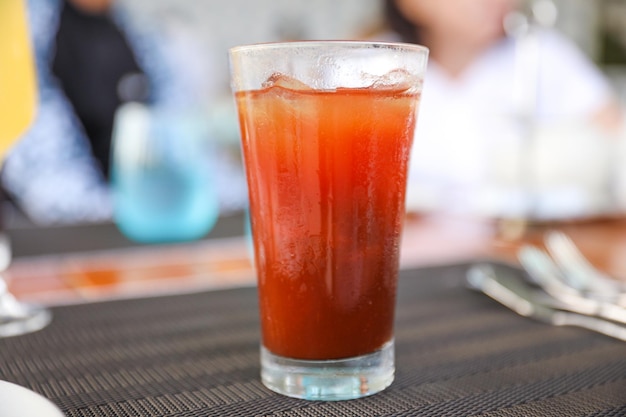 Un vaso de jugo de tomate en una mesa con una mujer al fondo