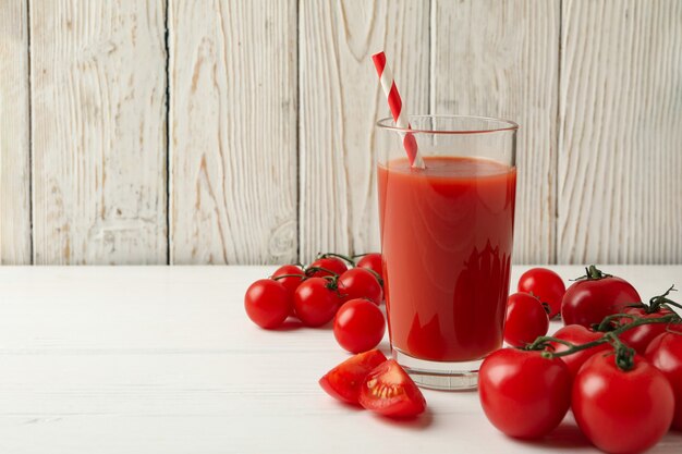 Vaso con jugo de tomate y paja y tomates en madera