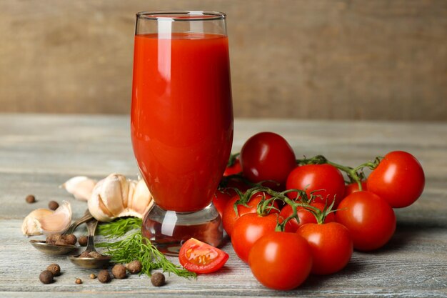 Vaso de jugo de tomate sabroso y tomates frescos en la mesa de madera