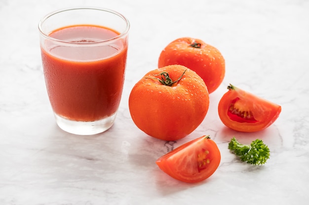 Vaso de jugo de tomate y tomates frescos en mesa de mármol
