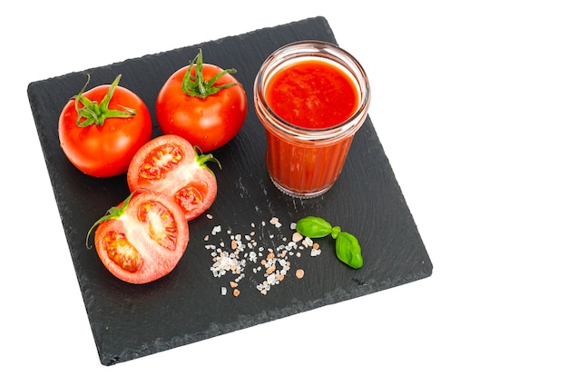 Vaso de jugo de tomate tomates rojos maduros en bandeja de piedra negra