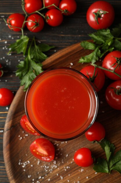 Foto vaso de jugo de tomate, tomates y sal sobre fondo de madera