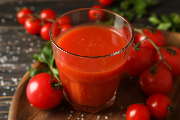 Vaso de jugo de tomate, tomates y sal sobre tabla de madera