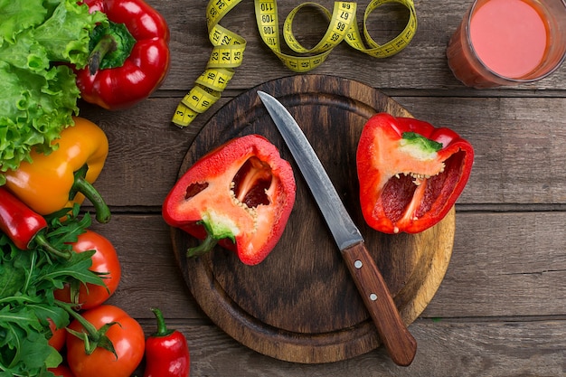 Vaso de jugo de tomate con verduras y cinta métrica en primer plano de la mesa de madera. En la tabla de cortar hay pimiento en rodajas. Copie el espacio. Vista superior