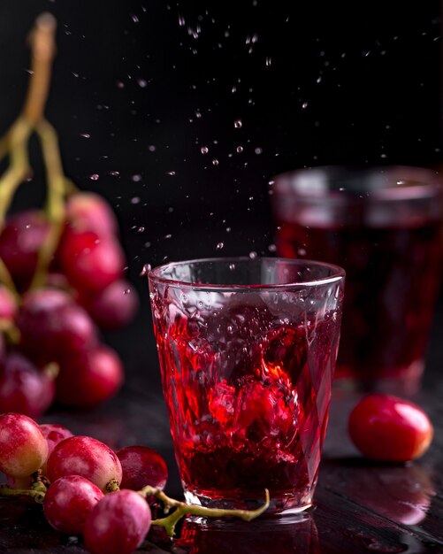 Un vaso de jugo de uva fresco, jugo de uva enlatado. Fondo oscuro, salpicaduras y gotas en un vaso.