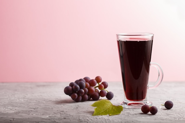 Vaso de jugo de uva roja sobre un fondo gris y rosa. Vista lateral