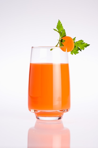 Vaso de jugo de vegetales orgánicos de naranja con una rodaja de zanahoria y hojas de perejil sobre un fondo blanco.