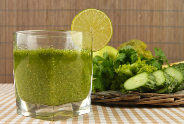 Vaso de jugo de vegetales verdes y verduras en mantel sobre fondo de bambú