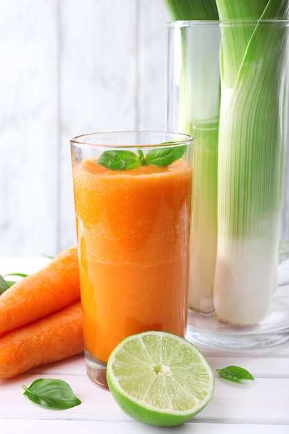 Vaso de jugo de zanahoria fresco cebolleta lima mechón de hierba y zanahoria en la mesa frente a la pared de madera