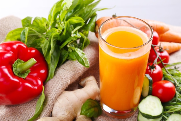 Vaso de jugo de zanahoria fresco y verduras en una servilleta de saqueo en una mesa de madera