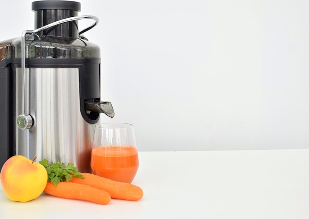 Un vaso de jugo de zanahoria junto a un exprimidor de zanahorias.