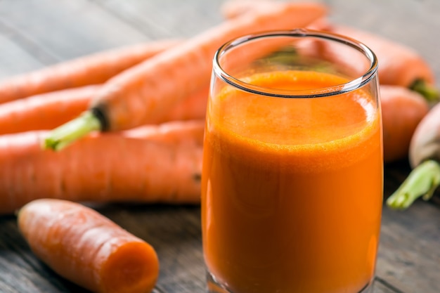 Un vaso de jugo de zanahoria recién exprimido sobre la vieja mesa de madera rústica