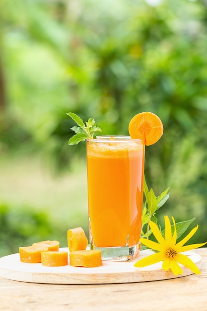 Vaso de jugo de zanahoria y zanahorias frescas sobre un fondo de madera con fondo verde de la naturaleza