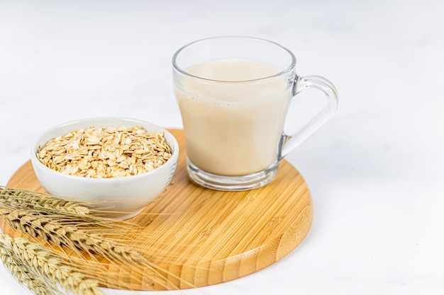 Vaso de leche de avena con copos de avena sobre fondo blanco de madera