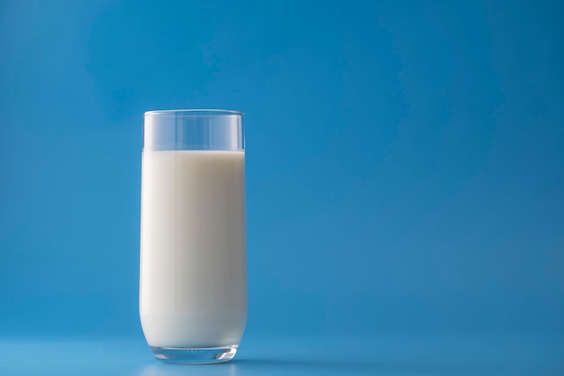 Vaso de leche blanca aislado sobre fondo azul, de cerca. Concepto de producto lácteo, espacio de copia