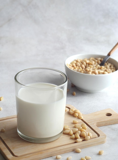 Un vaso de leche de cedro se encuentra sobre una tabla de madera sobre una mesa de hormigón Los piñones están dispersos cerca y un tazón de piñones está detrás