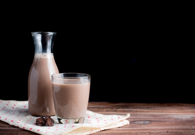 Vaso de leche con chocolate en la mesa de madera, fondo oscuro