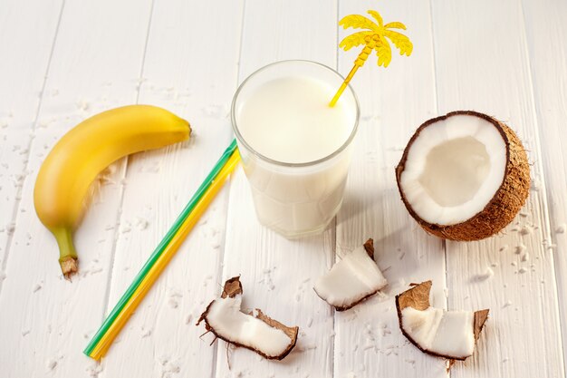 Vaso de leche de coco en la mesa de madera blanca, plátanos. Tropical. Enfoque selectivo