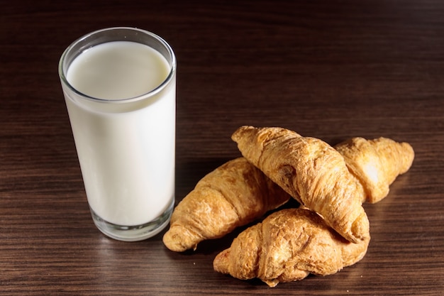 Vaso de leche y croissants recién hechos en la mesa de madera