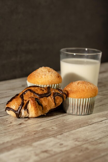 Vaso de leche con dos panecillos recién horneados y un croissant de chocolate en primer plano concepto de pastelería de desayuno