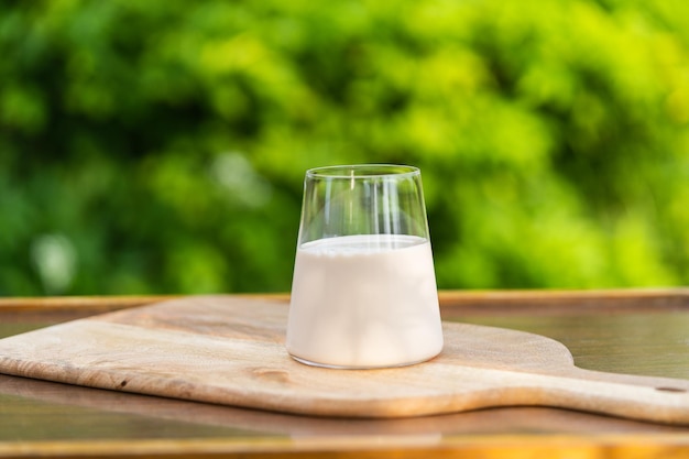 Un vaso de leche en un escritorio de madera contra el fondo natural verde desenfocado en un jardín