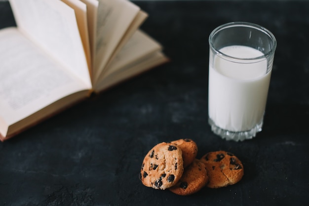 Vaso con leche fresca y galletas de chispas de chocolate sobre superficie oscura