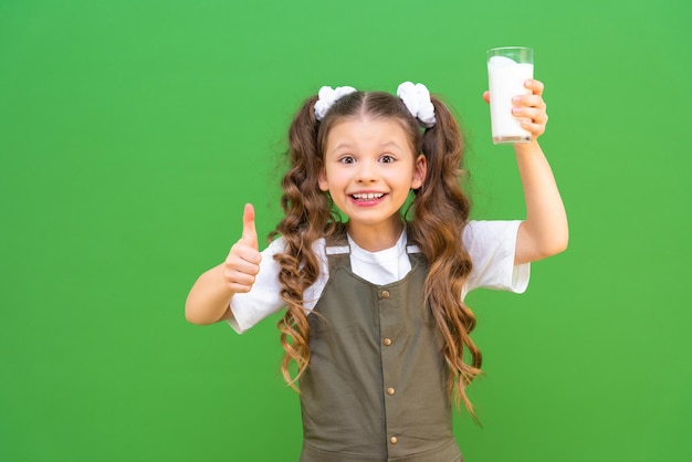 Un vaso de leche fresca en manos de una hermosa niña, el niño sostiene un vaso de kéfir y muestra un pulgar hacia arriba.