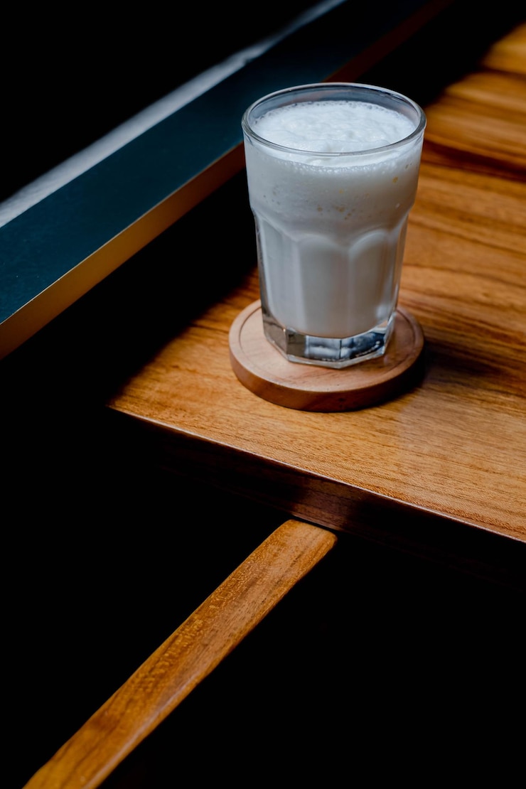Un vaso de leche fresca en un posavasos y una mesa de madera