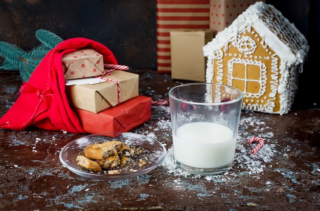 Vaso de leche y galletas caseras con chocolate a Santa en la mesa, adornos navideños,