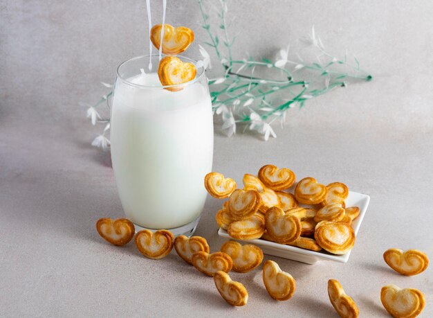 Foto vaso de leche con galletas cayendo sobre fondo claro