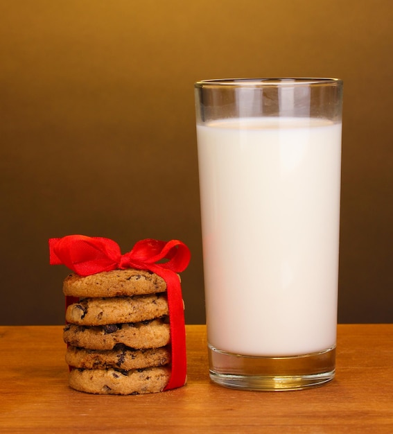 Vaso de leche y galletas en la mesa de madera sobre fondo marrón