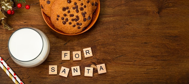 Un vaso de leche y galletas para santa claus sobre un fondo de madera vista superior regalo de navidad para