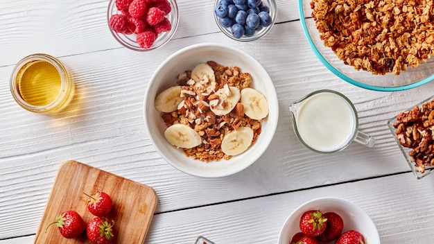 Un vaso de leche, jugosas bayas diferentes, miel y un plato con granola y rodajas de plátano