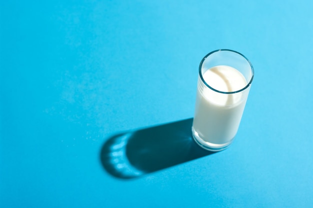 Foto vaso de leche bajo la luz brillante con sombra dura en fondo azul