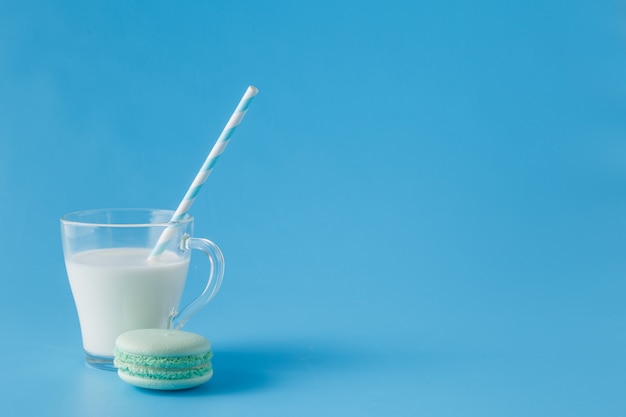 Vaso de leche con macarrones franceses sobre fondo azul.