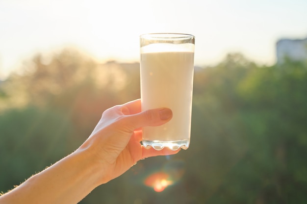 Vaso con leche en mano de mujer, puesta de sol de fondo