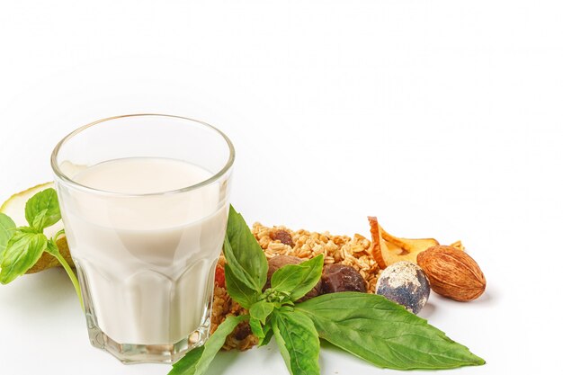 Un vaso de leche y muesli con frutas y hierbas sobre un fondo blanco