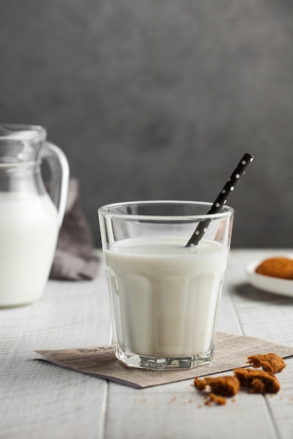 Vaso de leche con una pajita, galletas sobre una superficie gris