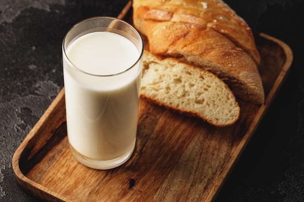 Vaso de leche con pan baguette en rodajas sobre plancha de madera