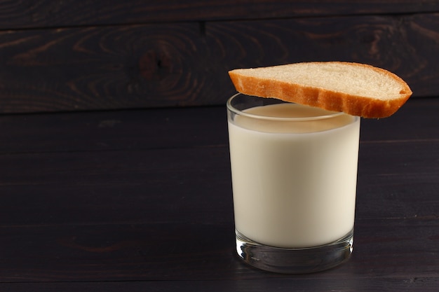 Foto un vaso de leche y pan sobre una superficie oscura.