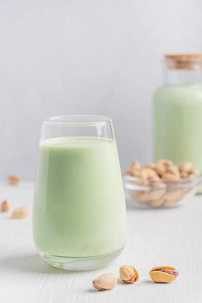 Vaso de leche de pistacho vegetariana a base de plantas frías servida en una mesa de madera blanca con tazón de nueces