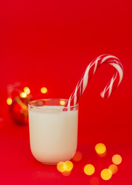 Vaso de leche con primer plano de dulces de Navidad sobre un fondo rojo con luces festivas. concepto de bebidas y golosinas navideñas para Santa Claus