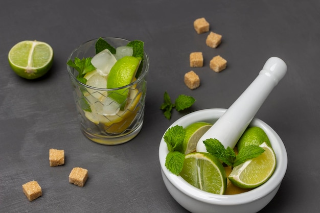 Vaso con lima menta y hielo Lima y menta en un mortero Media lima y trocitos de azúcar moreno sobre la mesa