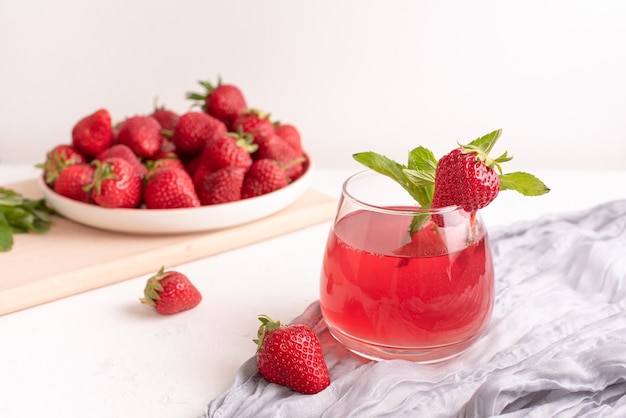 Vaso con limonada de fresa y fresas en una mesa con textiles sobre un fondo blanco, concepto de bebidas de verano, de cerca.