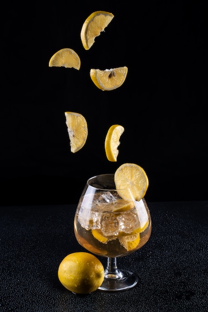 Foto vaso de limonada con hielo y rodajas de limón sobre un fondo negro
