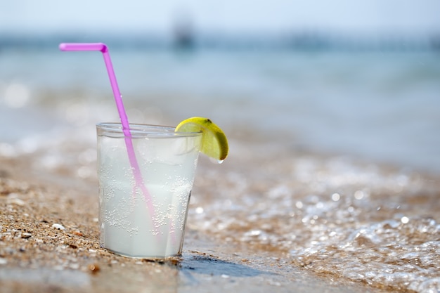 Vaso de limonada o agua en la playa por el mar