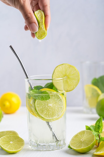 Vaso de limonada refrescante de rodajas de limón, agua con gas y menta servida con pajita en la mesa