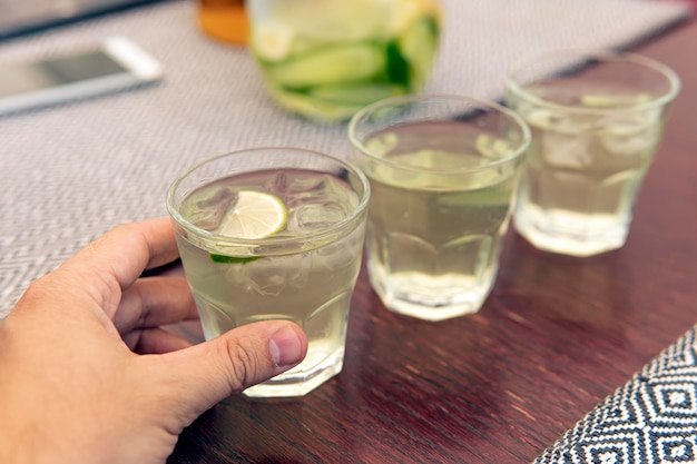 Un vaso con limonada rodajas de limón cubitos de hielo Bebida refrescante fría de verano en la mano de un hombre sobre la mesa en un café 3 vasos de limonada fresca y refrescante están sobre una mesa de madera en un café de verano